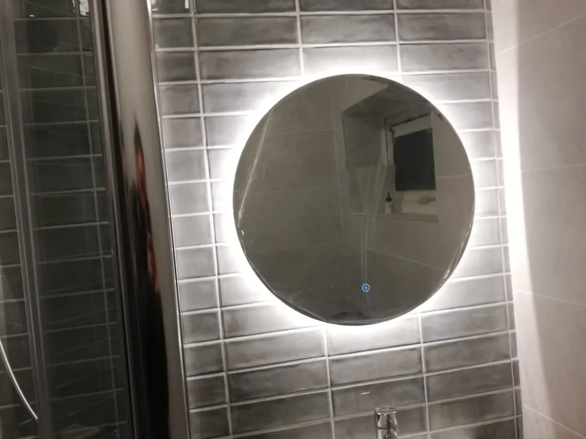 Round LED backlit mirror above wall-hung basin with grey brick tiles in London bathroom