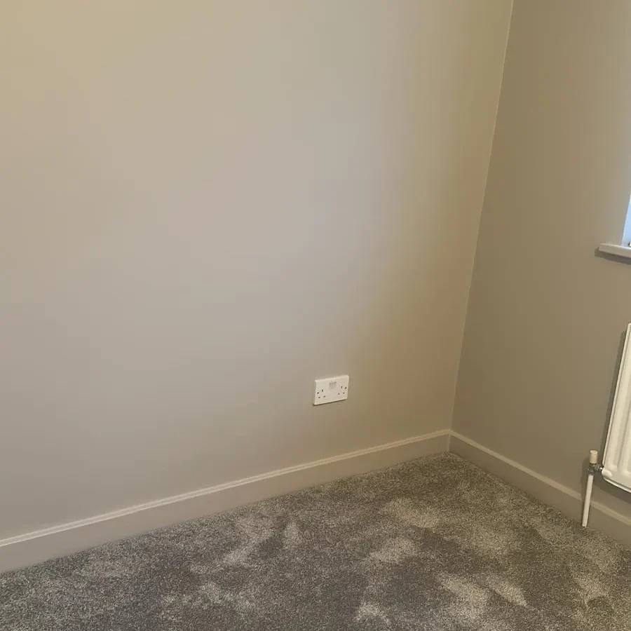 Freshly painted bedroom with new grey carpet and radiator after renovation