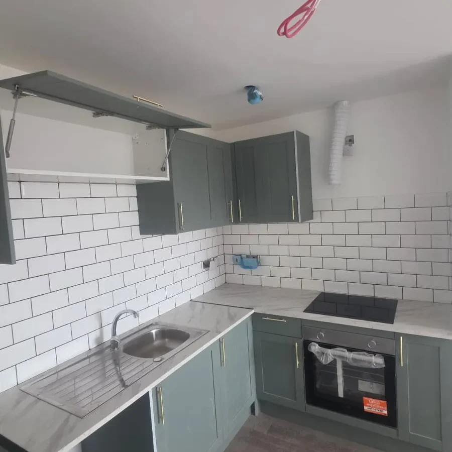 Green shaker kitchen with white metro tiles, marble-effect worktop and integrated oven nearing completion