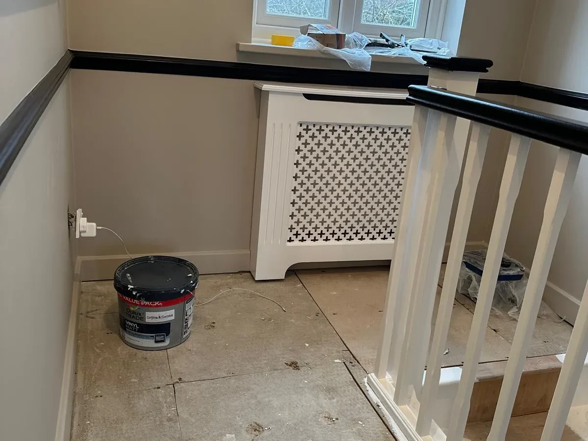 Stair landing mid-renovation with radiator cover, black dado rail and paint tub