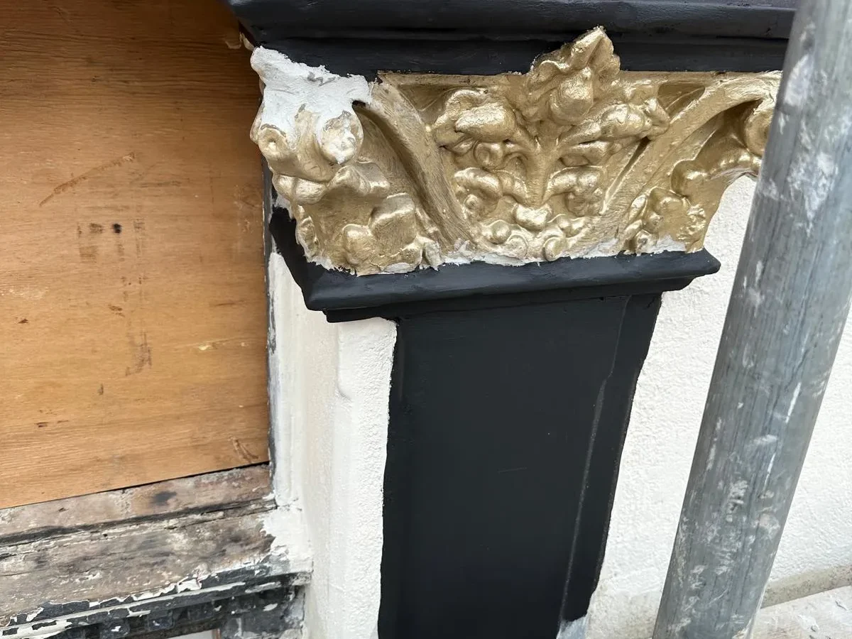 Restored ornate gilded corbel with fresh black and magenta paintwork on shopfront exterior