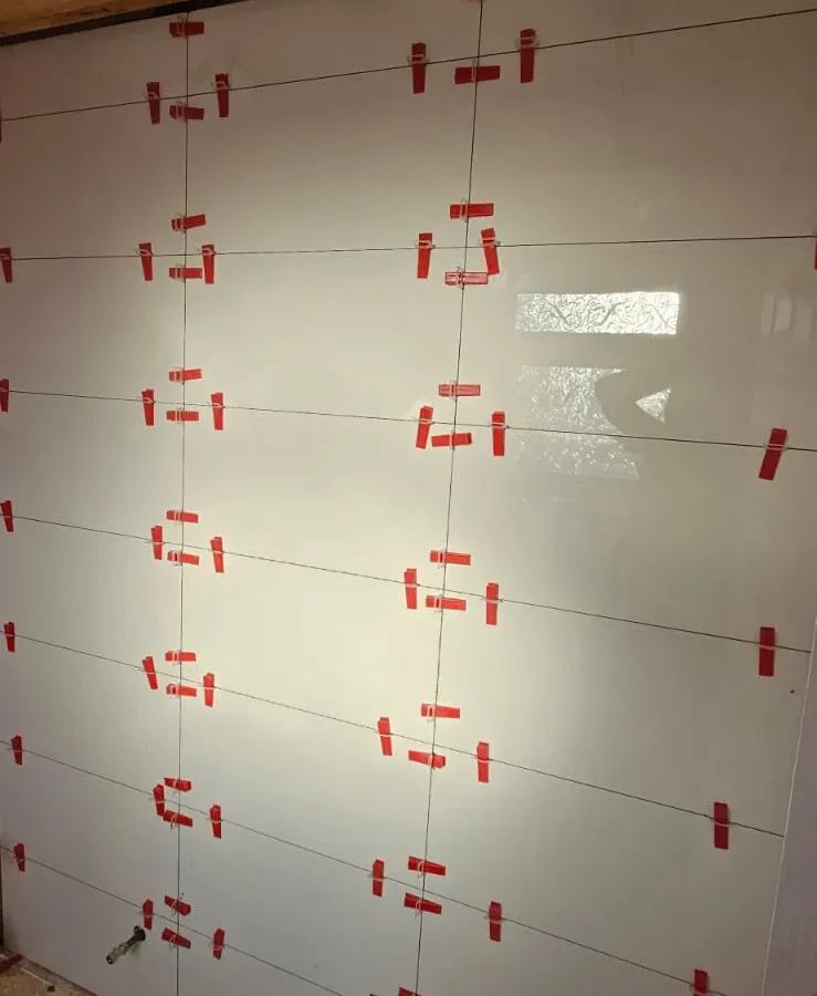 White gloss wall tiles being installed with red levelling clips during renovation