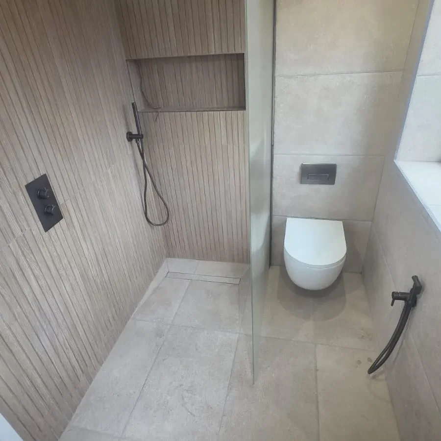 Modern wet room with wood-effect tiles, wall-hung toilet, black taps and glass shower screen